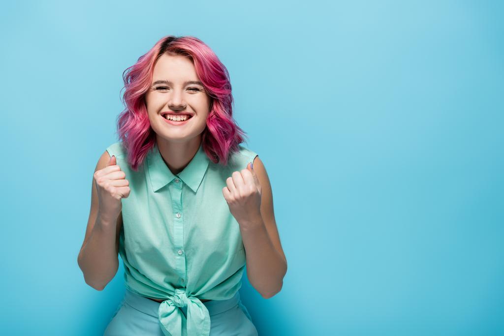 young woman with pink hair showing yeah gesture on blue background - Photo, Image