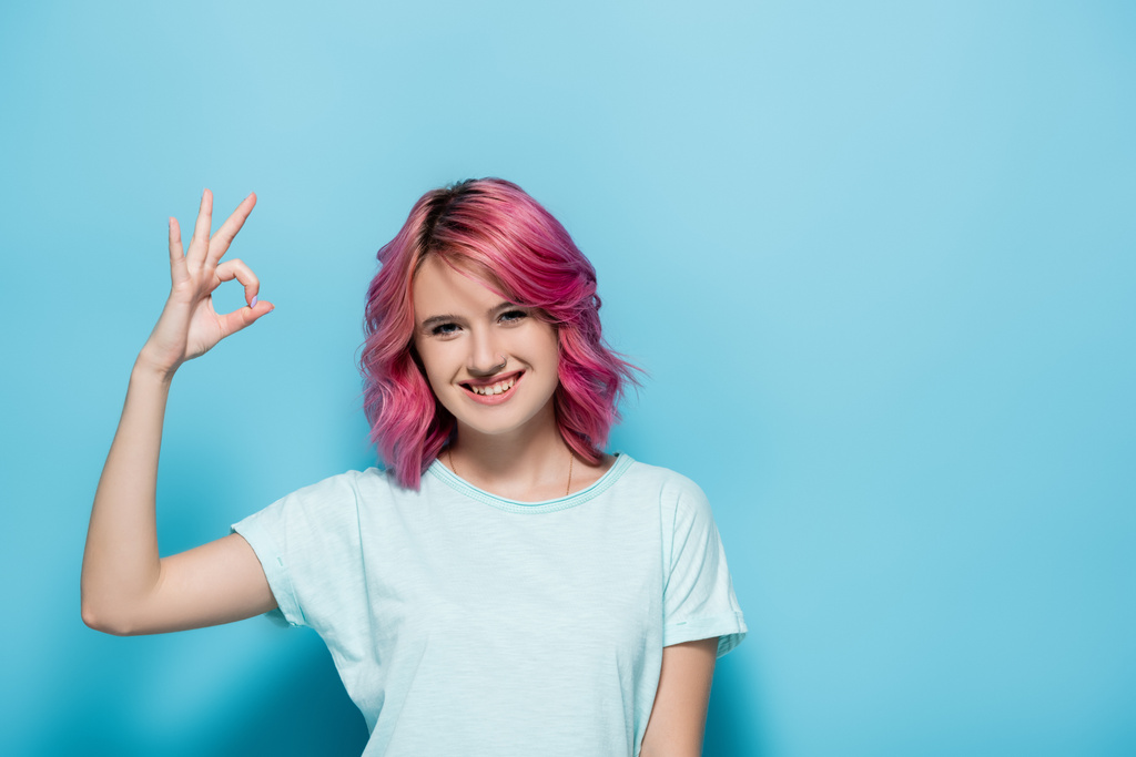 mujer joven con el pelo rosa mostrando signo ok sobre fondo azul - Foto, imagen