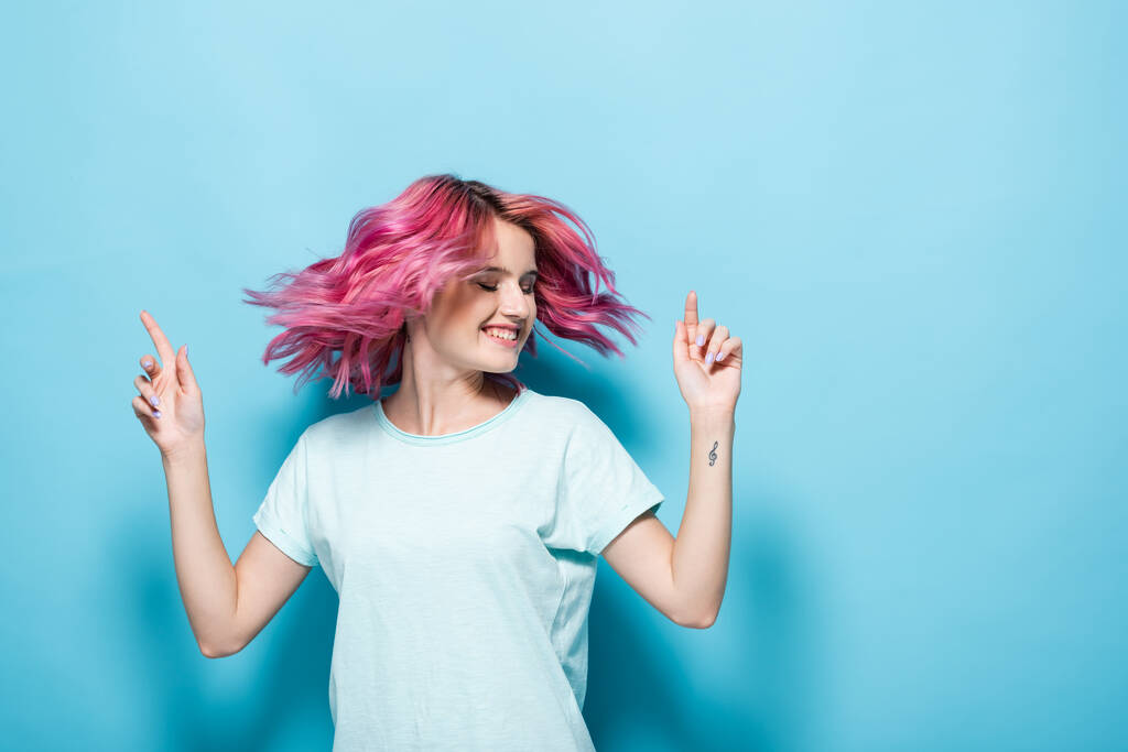 青い背景にピンクの髪を振っている若い女性 - 写真・画像