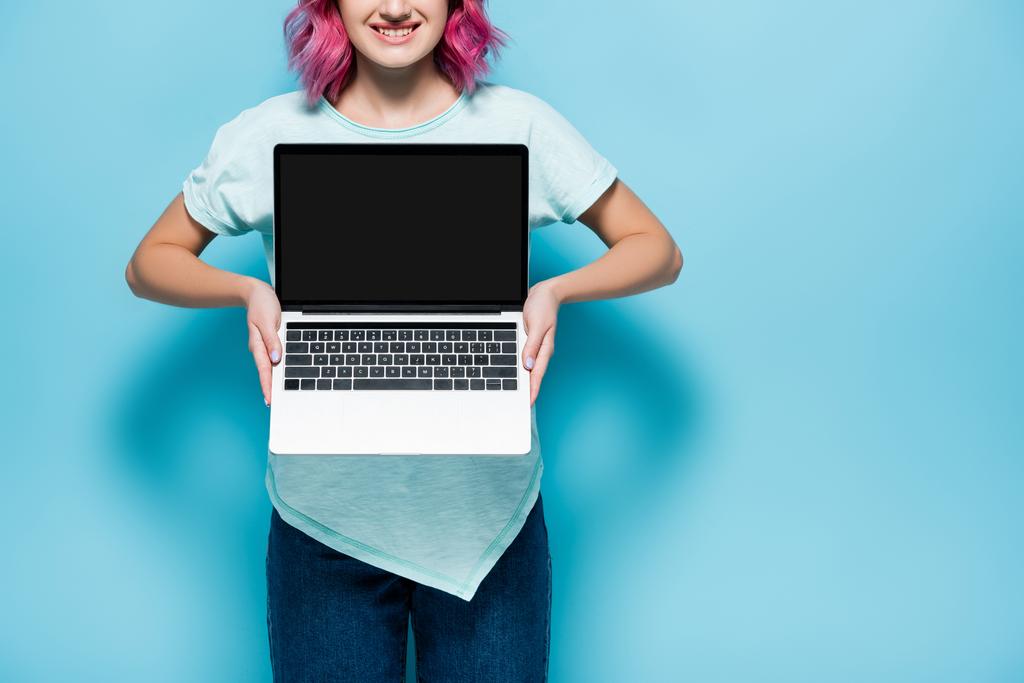 corte vista de jovem mulher com cabelo rosa mostrando laptop com tela em branco no fundo azul - Foto, Imagem