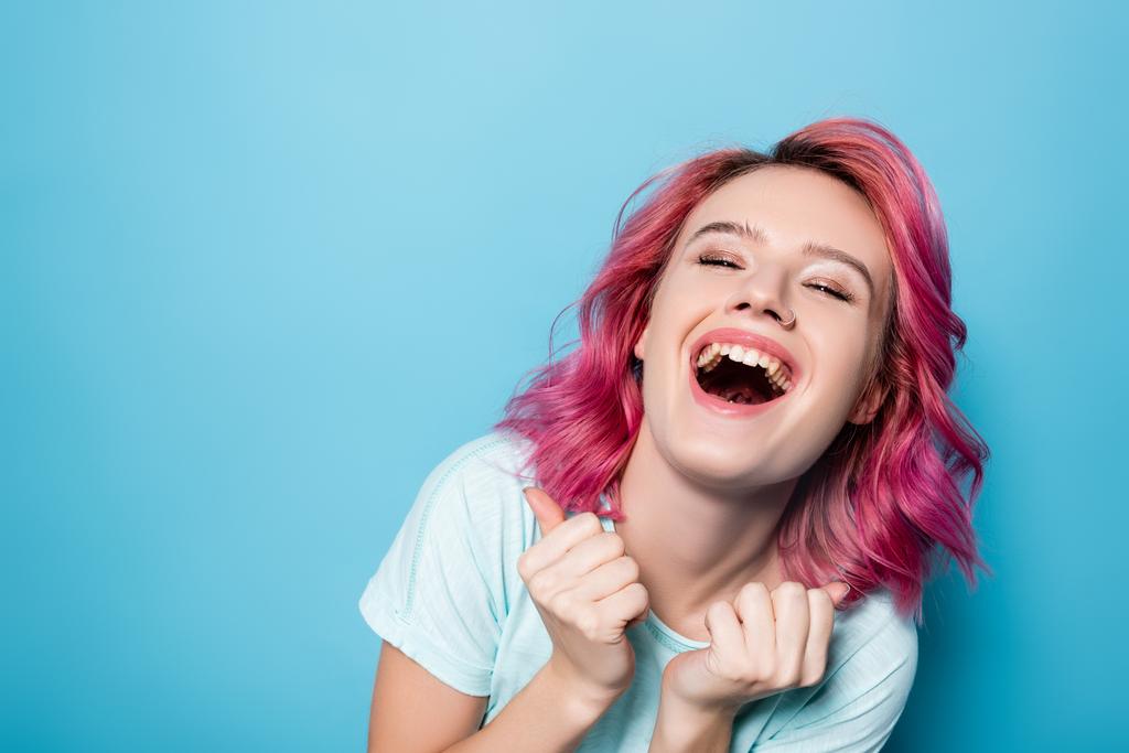 молода жінка з рожевим волоссям сміється на синьому фоні
 - Фото, зображення