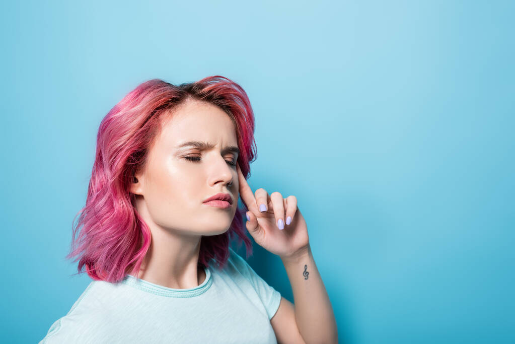 mujer joven reflexiva con pelo rosa y tatuaje sobre fondo azul - Foto, imagen