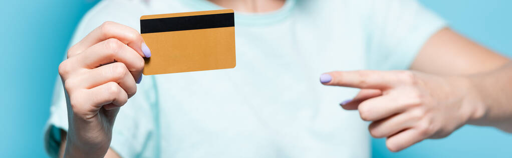 messa a fuoco selettiva della giovane donna che punta la carta di credito su sfondo blu, scatto panoramico - Foto, immagini