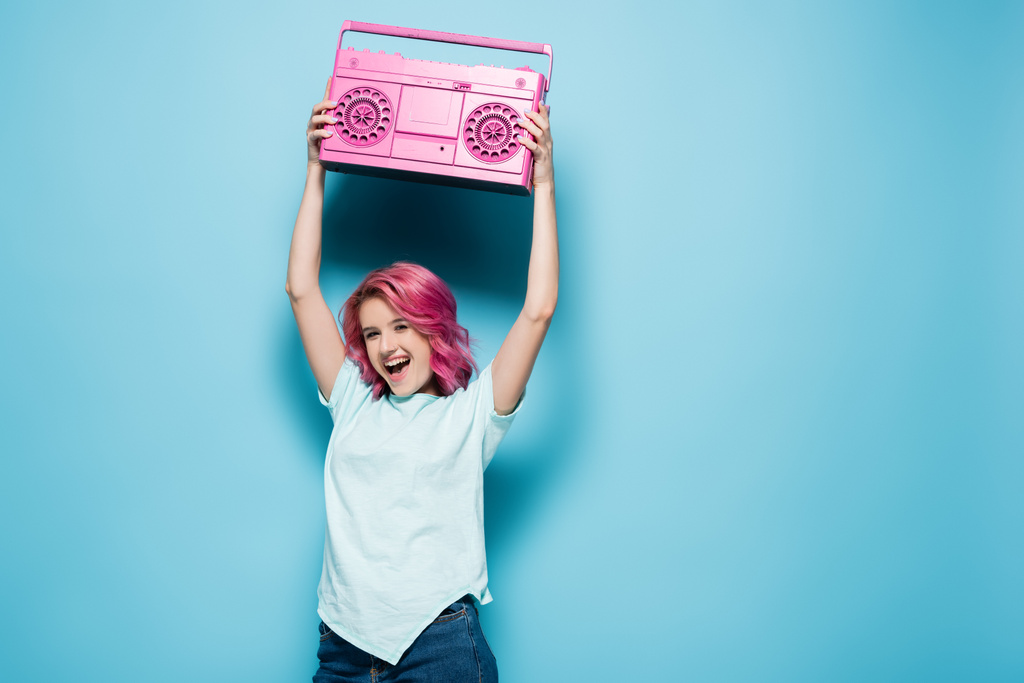 young woman with pink hair holding vintage tape recorder on blue background - Photo, Image
