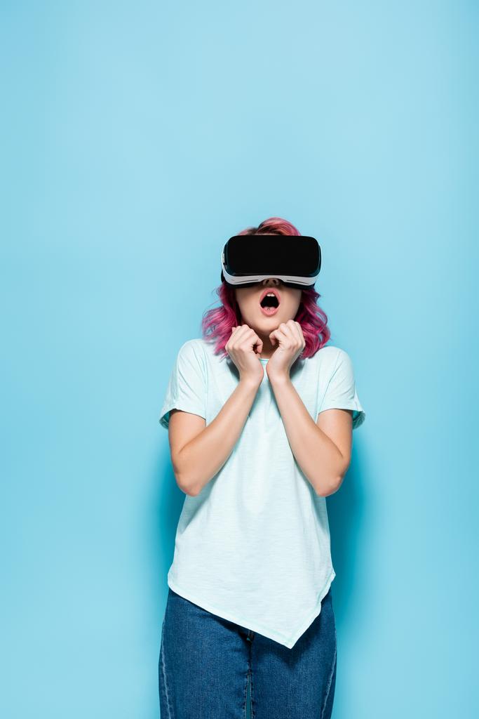 scared young woman with pink hair in vr headset on blue background - Photo, Image