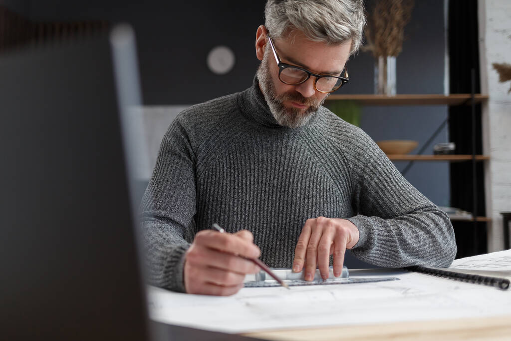 Architect drawing blueprints in office. Engineer sketching a construction project. Architectural plan. Close-up portrait of handsome bearded man concentrated on work. Business construction concept - Photo, Image