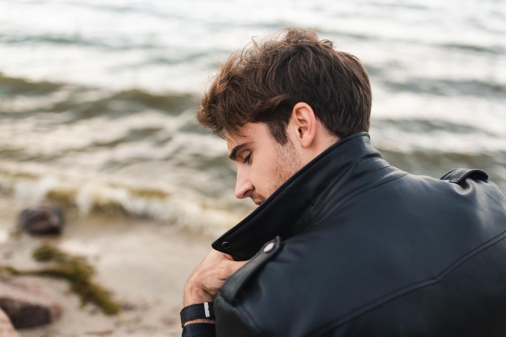 Widok z tyłu młody człowiek w czarnej skórzanej kurtce na wybrzeżu morza  - Zdjęcie, obraz