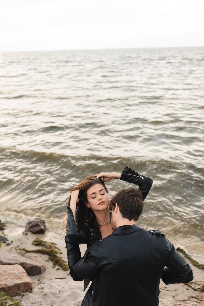 Vue grand angle de jeune homme embrasser petite amie en cuir Jacker sur la plage près de la mer  - Photo, image