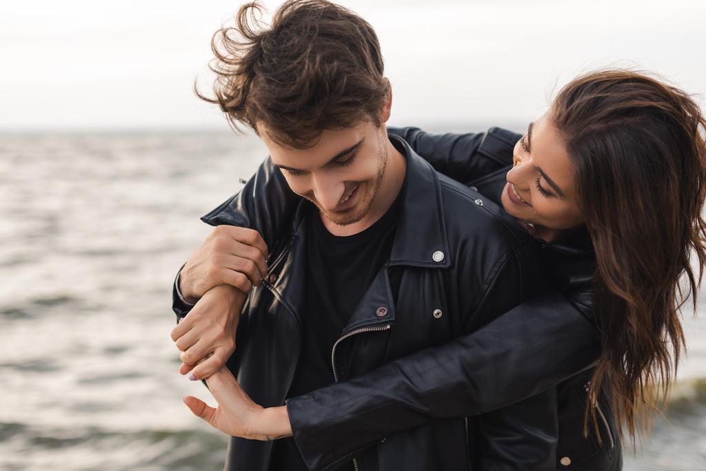 Brunette nainen halaus poikaystävä nahkatakki lähellä merta  - Valokuva, kuva