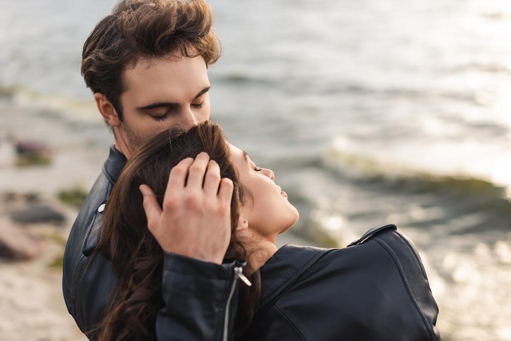 Uomo baciare e toccare i capelli della donna in giacca di pelle sulla spiaggia  - Foto, immagini