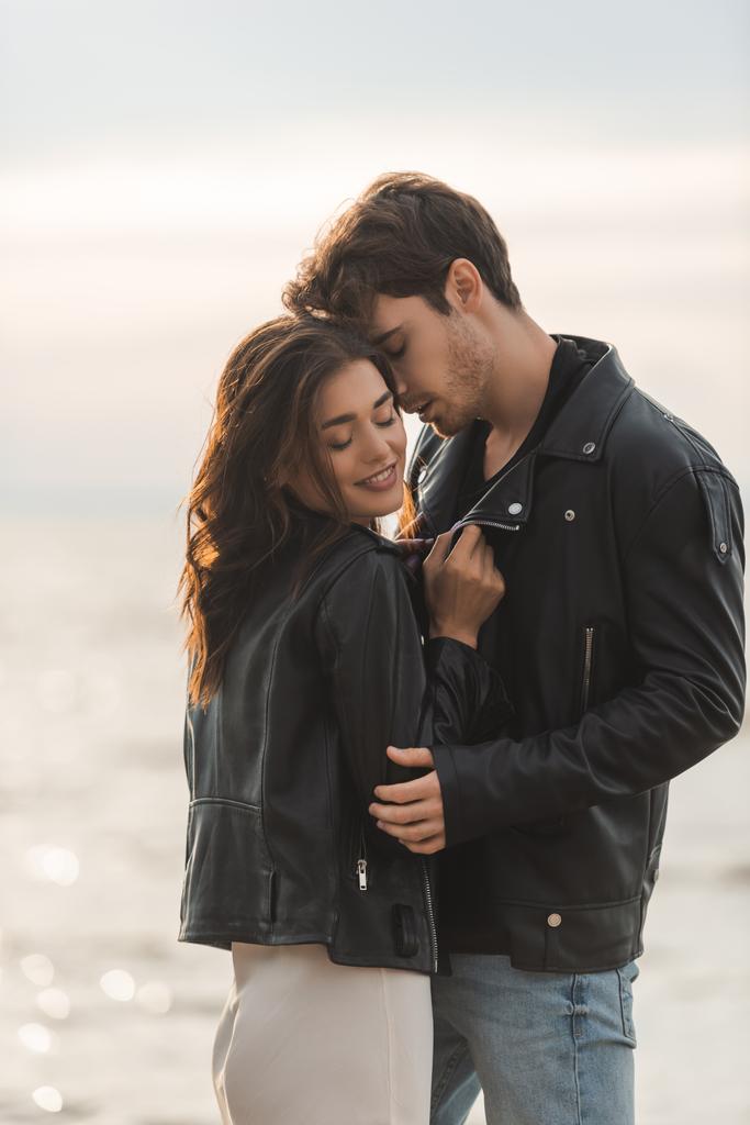 Brunette woman in dress and leather jacket standing near boyfriend and sea - Photo, Image