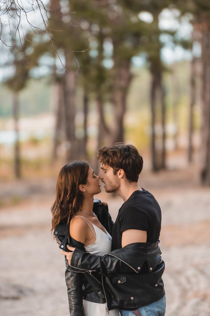 Vista lateral do homem beijando e tirando jaqueta de couro da namorada na floresta  - Foto, Imagem
