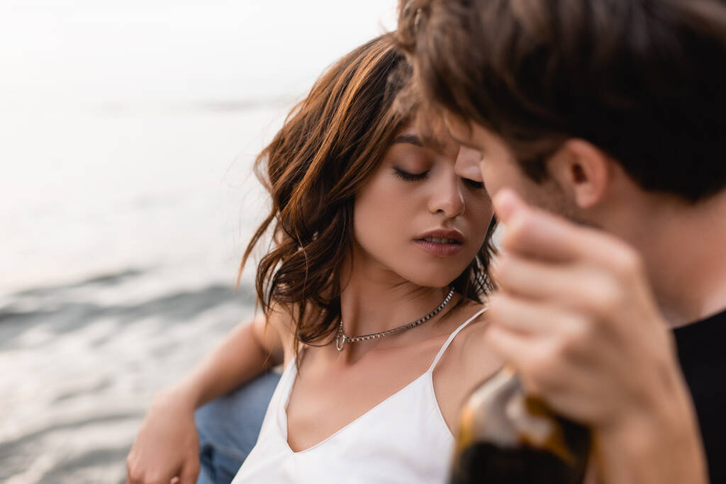 Selective focus of woman holding bottle of wine near boyfriend and sea   - Photo, Image