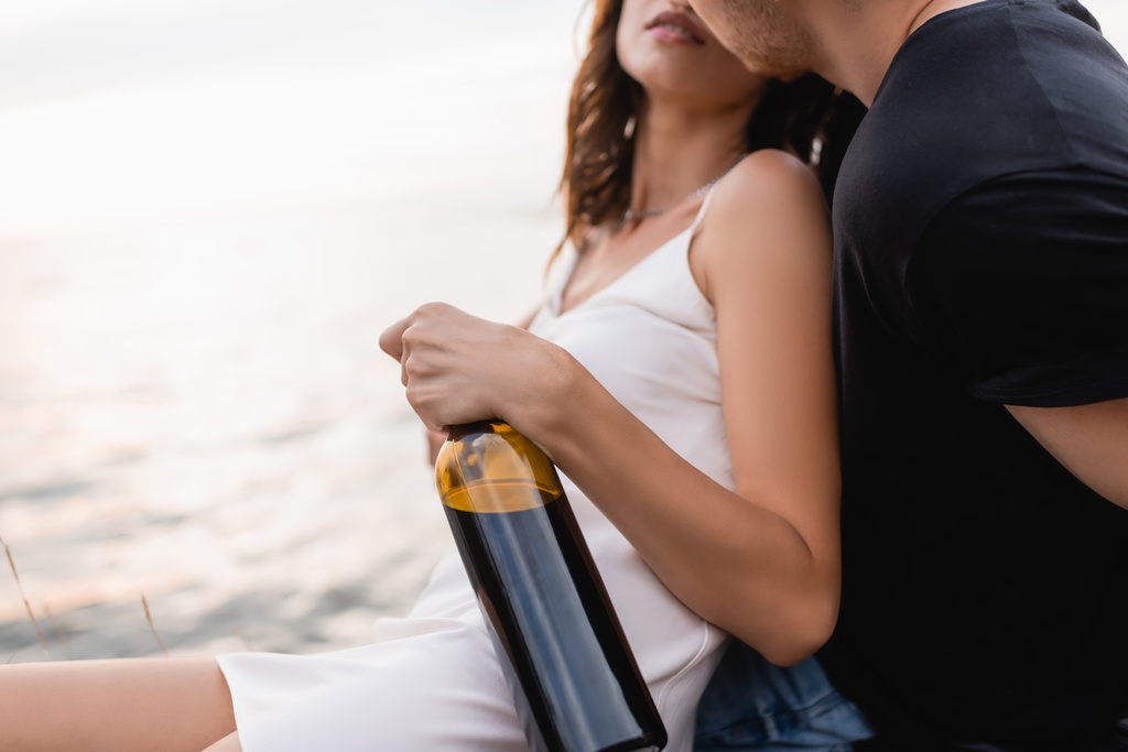 Deniz kenarında bir şişe şarapla kız arkadaşını öpen adam görüntüsü.  - Fotoğraf, Görsel