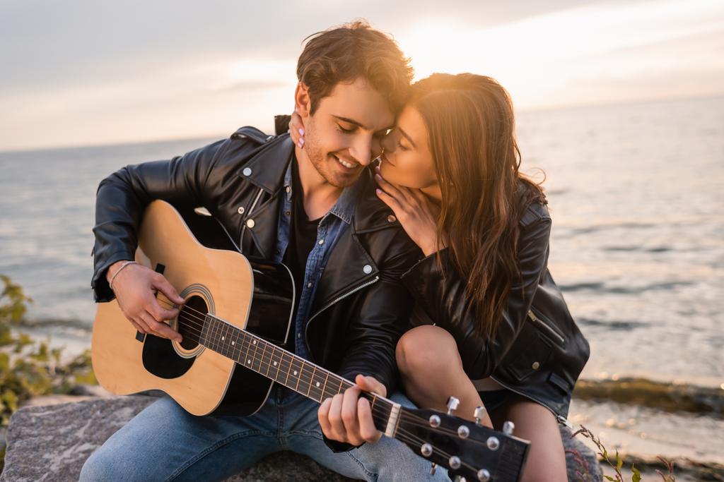 若いです女性接吻ボーイフレンド遊びますアコースティックギターオン海辺で日没  - 写真・画像