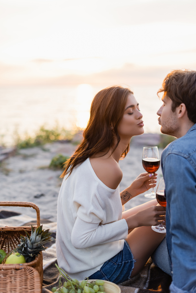 Foco seletivo de jovens casais beijando enquanto seguram copos de vinho durante piquenique na praia  - Foto, Imagem