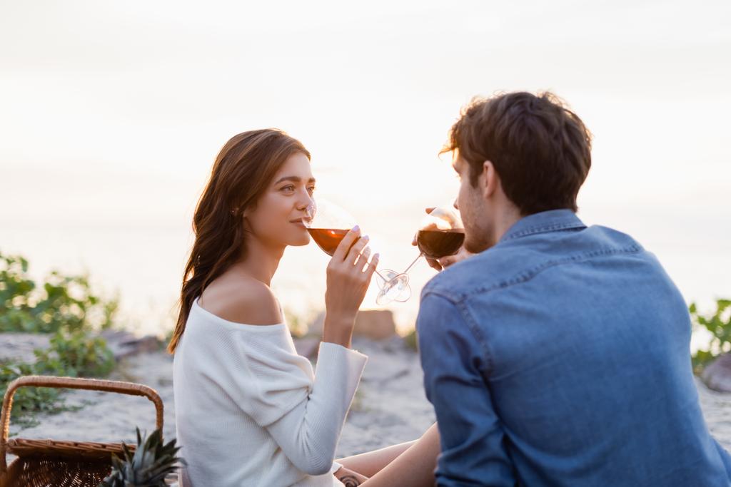 Foco seletivo de mulher bebendo vinho com namorado durante piquenique na praia  - Foto, Imagem