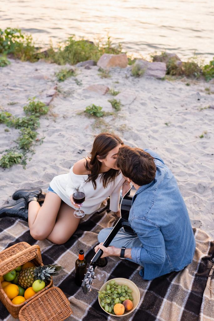 Paar mit Wein und Akustikgitarre küsst sich abends am Strand  - Foto, Bild