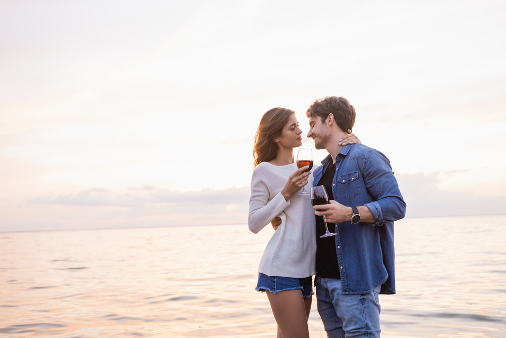Jonge vrouw met glas wijn en aanraken vriendje in de buurt van de zee  - Foto, afbeelding