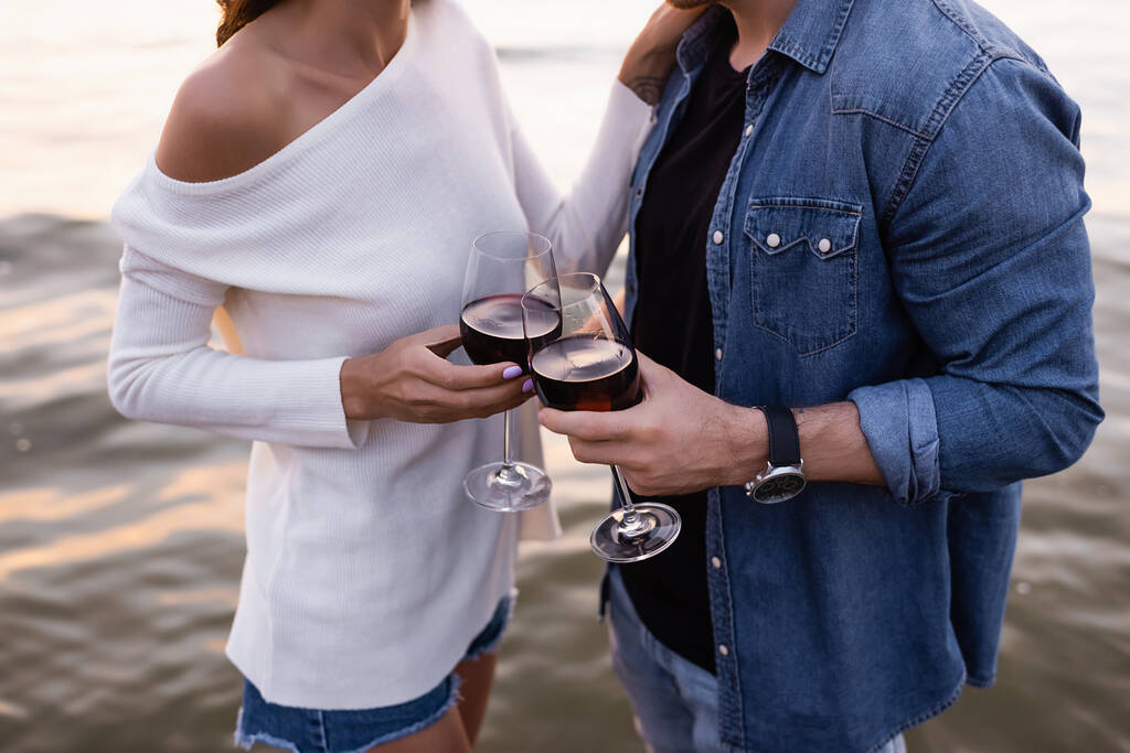 Oříznutý pohled na mladý pár držící sklenice vína v blízkosti moře  - Fotografie, Obrázek