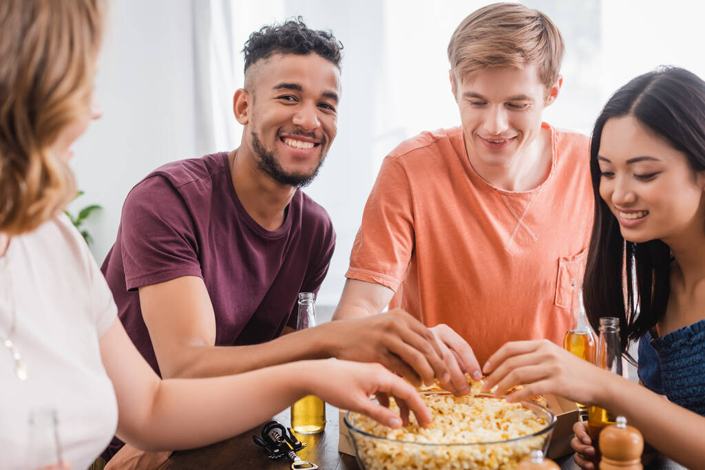 enfoque selectivo de amigos multiculturales emocionados tomando palomitas de maíz del tazón durante la fiesta - Foto, imagen