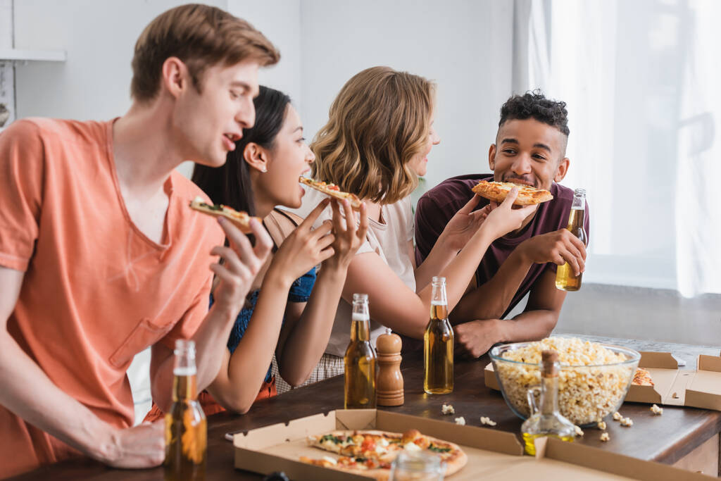 selektywne skupienie się na radosnych, wieloetnicznych przyjaciołach jedzących pizzę podczas imprezy - Zdjęcie, obraz