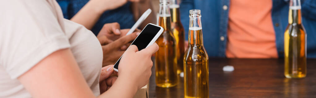 частковий вид на багатоетнічні друзі спілкуються на смартфонах біля пива під час вечірки, горизонтальні врожаї
 - Фото, зображення