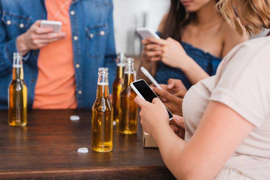 abgeschnittene Ansicht multiethnischer Freunde, die während einer Party in der Nähe von Bier auf Smartphones chatten - Foto, Bild