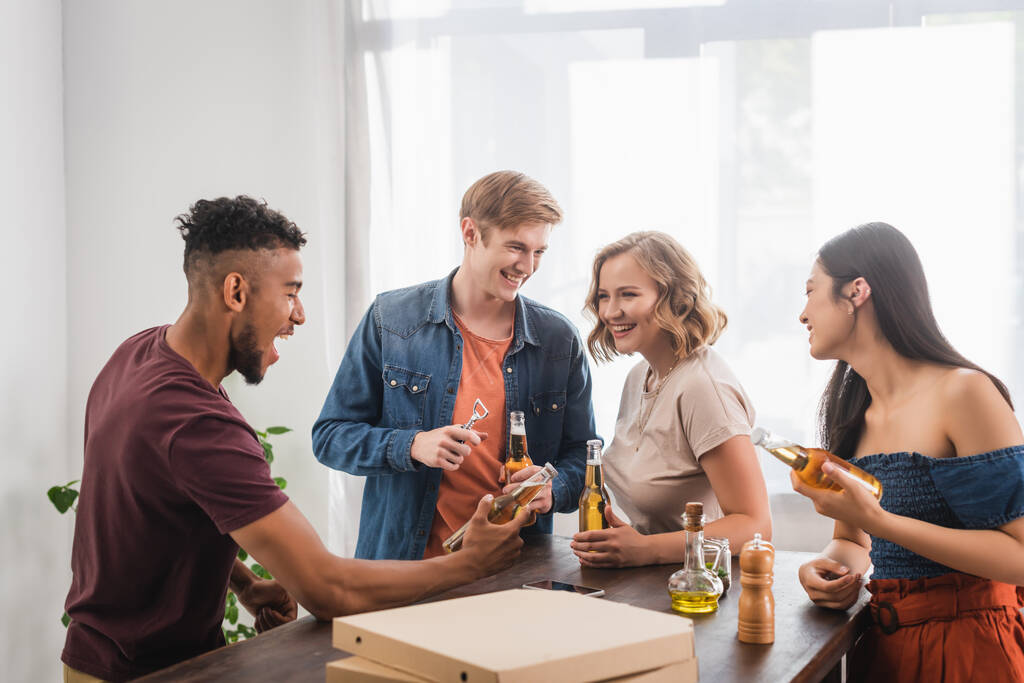 excited african american man holding bottle of beer near multiethnic friends during party - Photo, Image