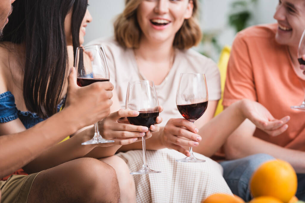 селективное внимание мультикультурных друзей, держащих бокалы красного вина во время вечеринки - Фото, изображение