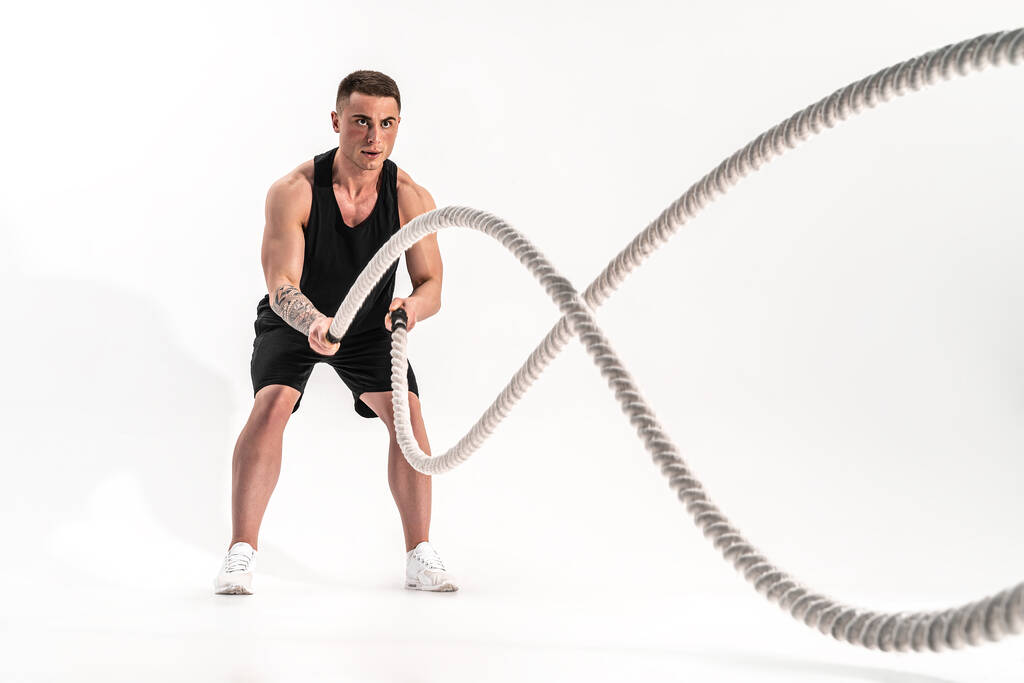 Hombre musculoso atractivo haciendo ejercicio con cuerdas pesadas. Foto de un hombre guapo en ropa deportiva aislado sobre fondo blanco - Foto, Imagen