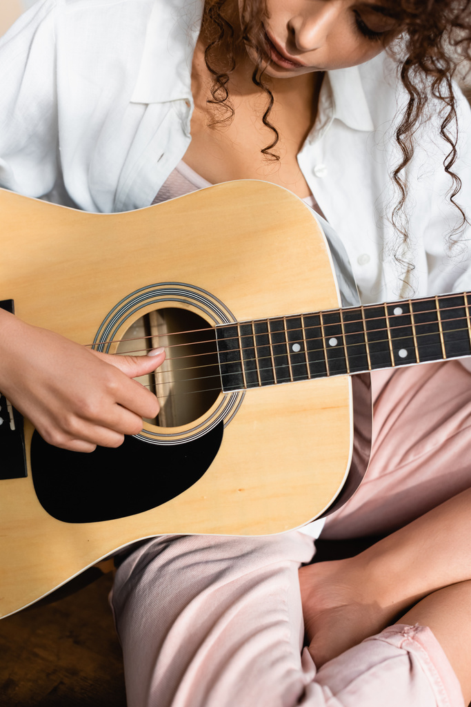 vue recadrée de jeune femme bouclée jouant de la guitare acoustique à la maison - Photo, image