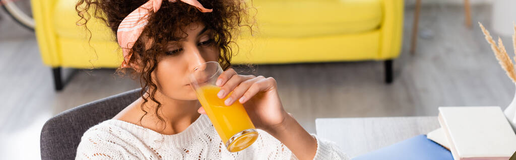 horizontales Bild einer lockigen Frau, die frischen Orangensaft trinkt  - Foto, Bild