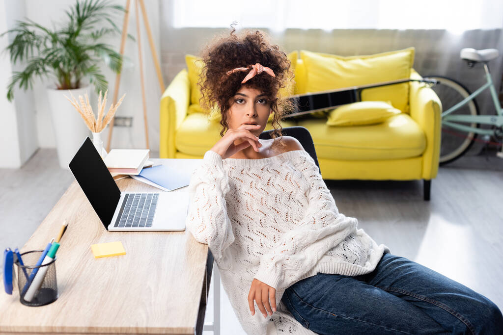 donna riccia seduta vicino al computer portatile con schermo bianco sulla scrivania - Foto, immagini