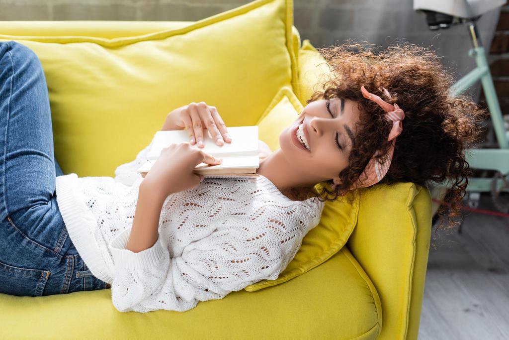 високий кут зору збудженої молодої жінки, що тримає книгу, лежачи на дивані у вітальні
  - Фото, зображення