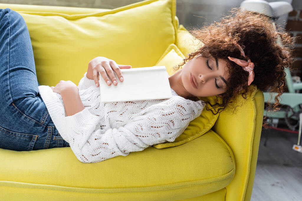 kihara nuori nainen nukkuu kirjan kanssa olohuoneessa  - Valokuva, kuva