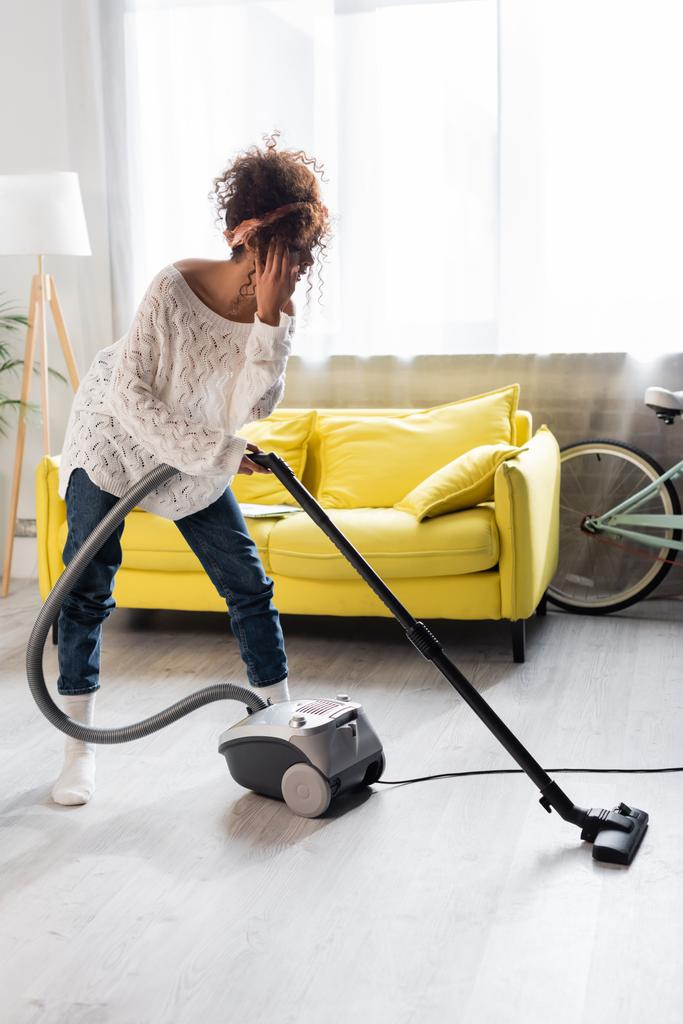 jeune femme en chaussettes en utilisant l'aspirateur tout en nettoyant la maison - Photo, image
