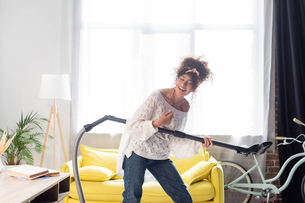 donna riccia divertirsi, tenendo aspirapolvere e pulizia a casa - Foto, immagini