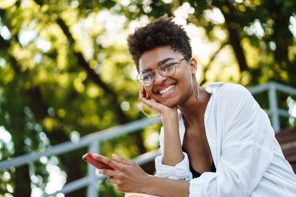 Mutlu Afrikalı bir kadının parkta oturmuş cep telefonuyla sohbet ederken fotoğrafı. - Fotoğraf, Görsel