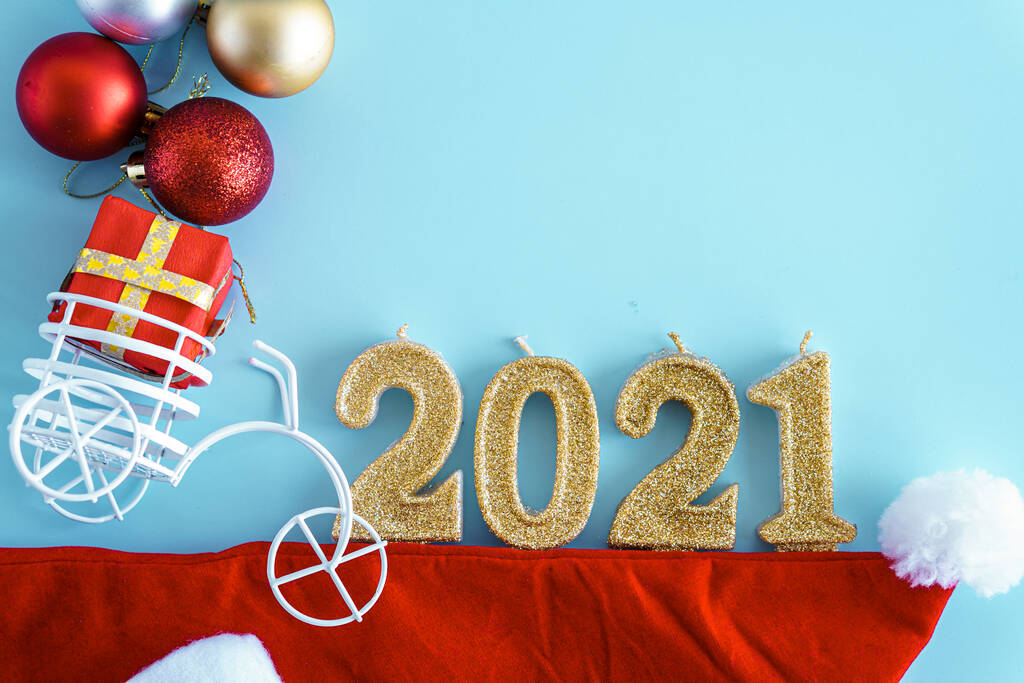 Navidad, invierno, concepto de año nuevo - Fondo azul de Navidad con juguetes de oro rojo y árbol blanco, sombrero de Santa, velas número 2021 y bicicleta de juguete con regalo en el maletero. Flatly, vista superior, arriba. Copiar espacio - Foto, Imagen