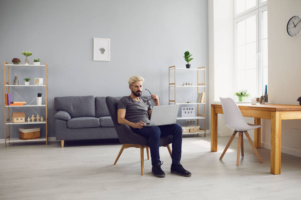 Sorrindo homem sentado na cadeira com laptop e trabalhando online em casa - Foto, Imagem