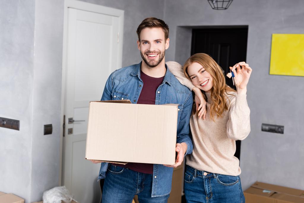 femme joyeuse tenant les clés près du petit ami avec boîte en carton  - Photo, image