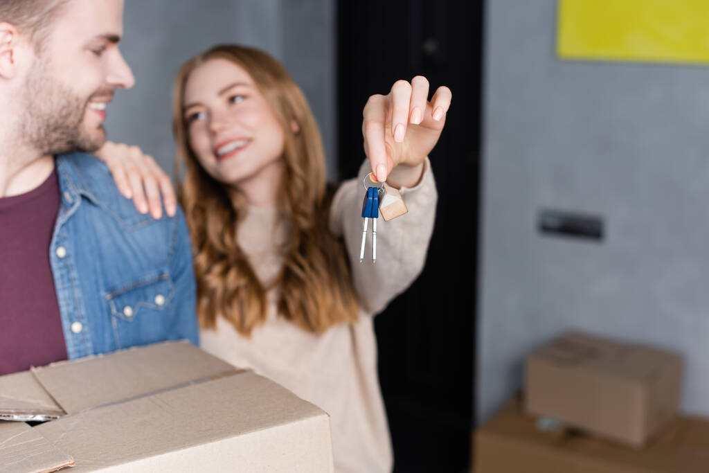 selective focus of woman holding keys and looking at boyfriend with box  - Photo, Image