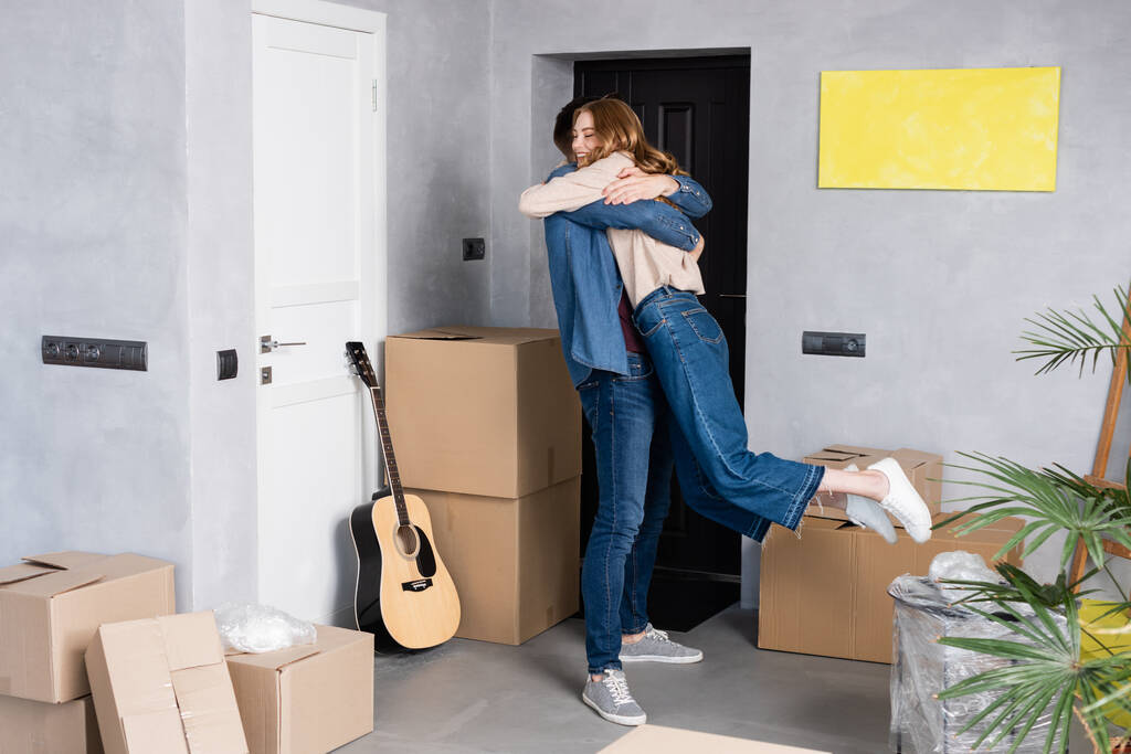 joyful woman hugging with boyfriend near carton boxes and acoustic guitar - Photo, Image