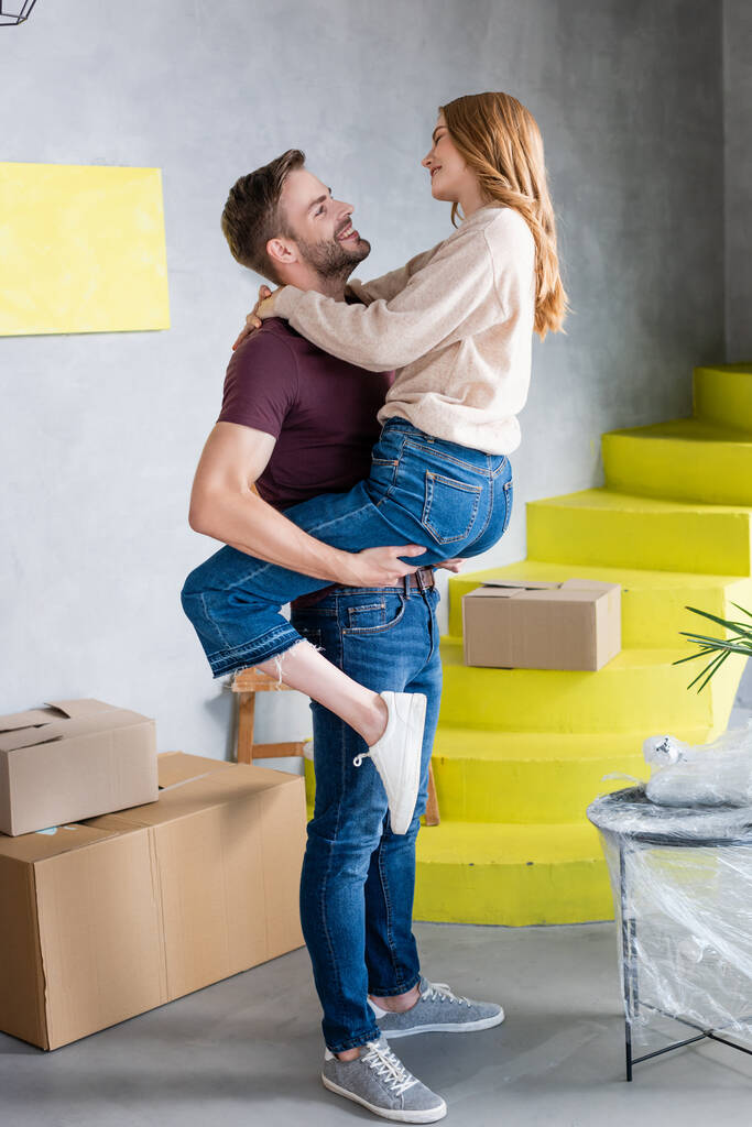 man holding in arms and looking at joyful girlfriend in new home - Photo, Image