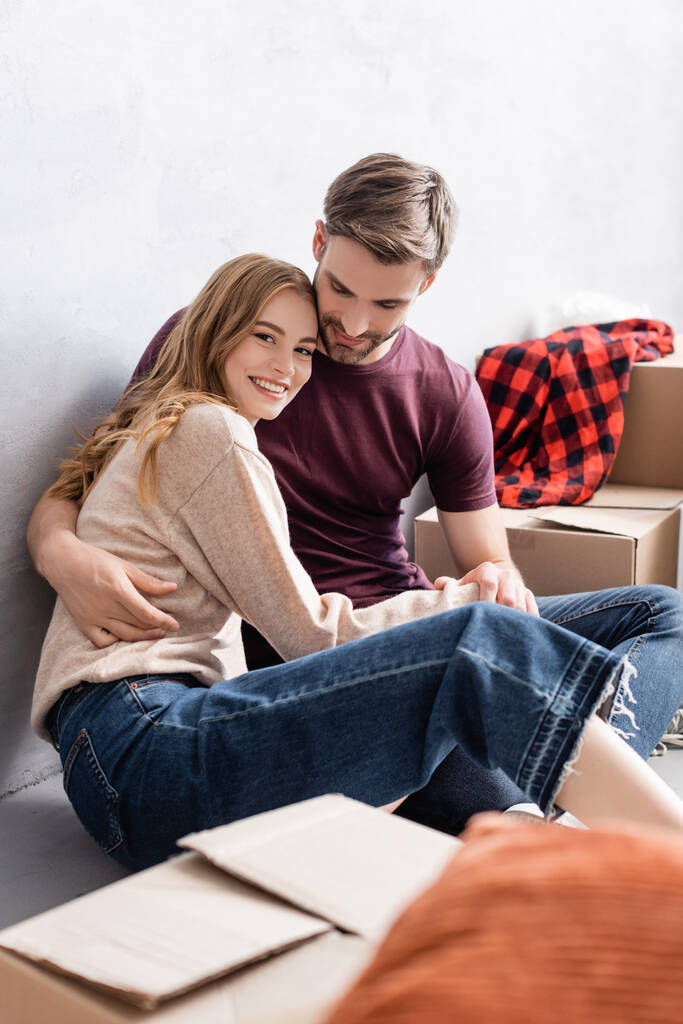 homem satisfeito sentado de chão e abraçando namorada perto de caixas - Foto, Imagem
