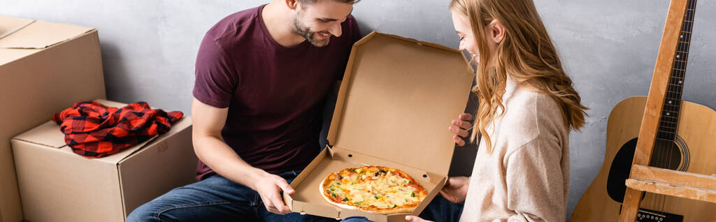 panoramatický koncept muže a ženy při pohledu na pizzu v papírové krabici - Fotografie, Obrázek