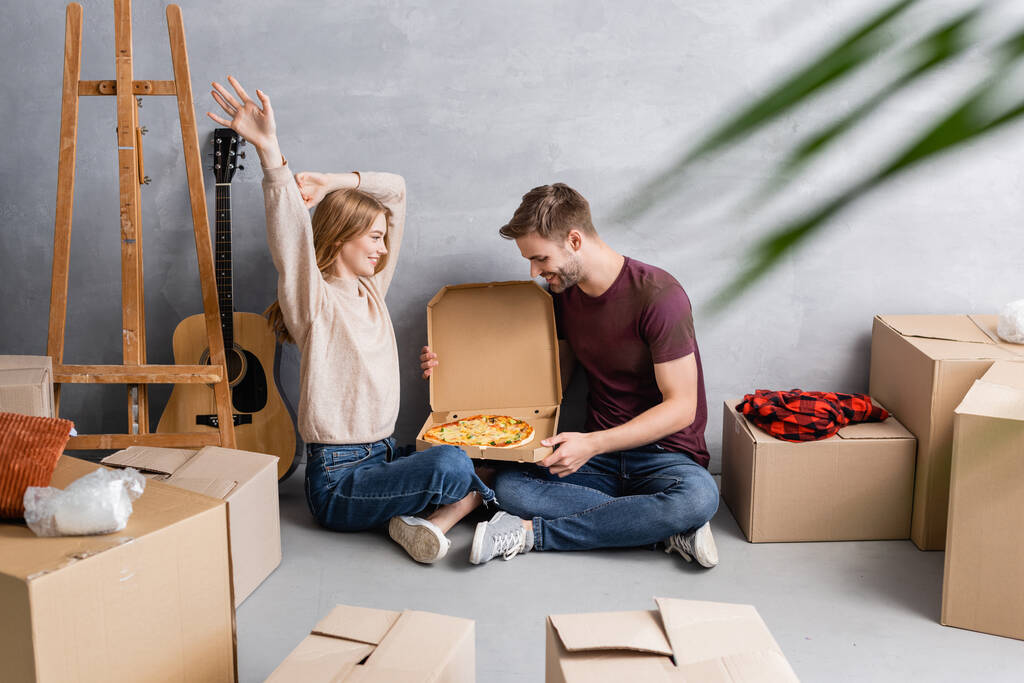 вибірковий фокус радісної пари, дивлячись на піцу біля картонних коробок та акустичну гітару
 - Фото, зображення