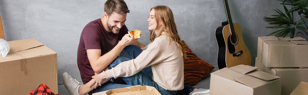 панорамний урожай задоволеного чоловіка, що тримає піцу біля жінки та картонні коробки
 - Фото, зображення