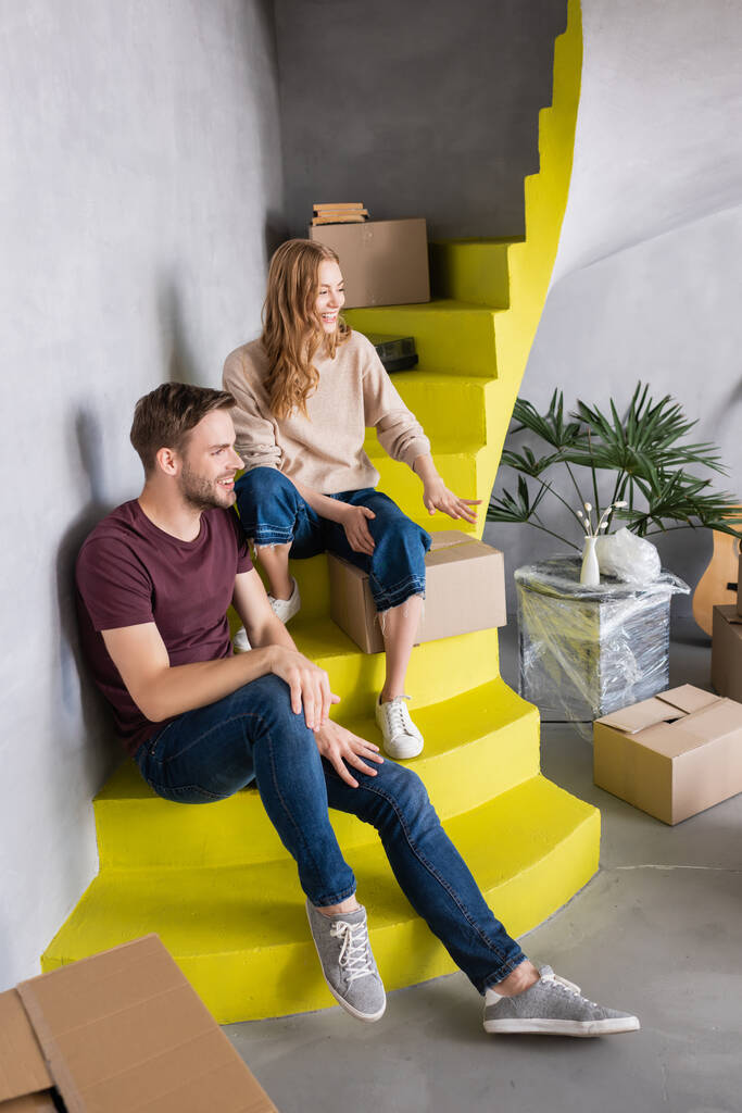 радісна пара дивиться на коробки, сидячи на жовтих сходах
 - Фото, зображення